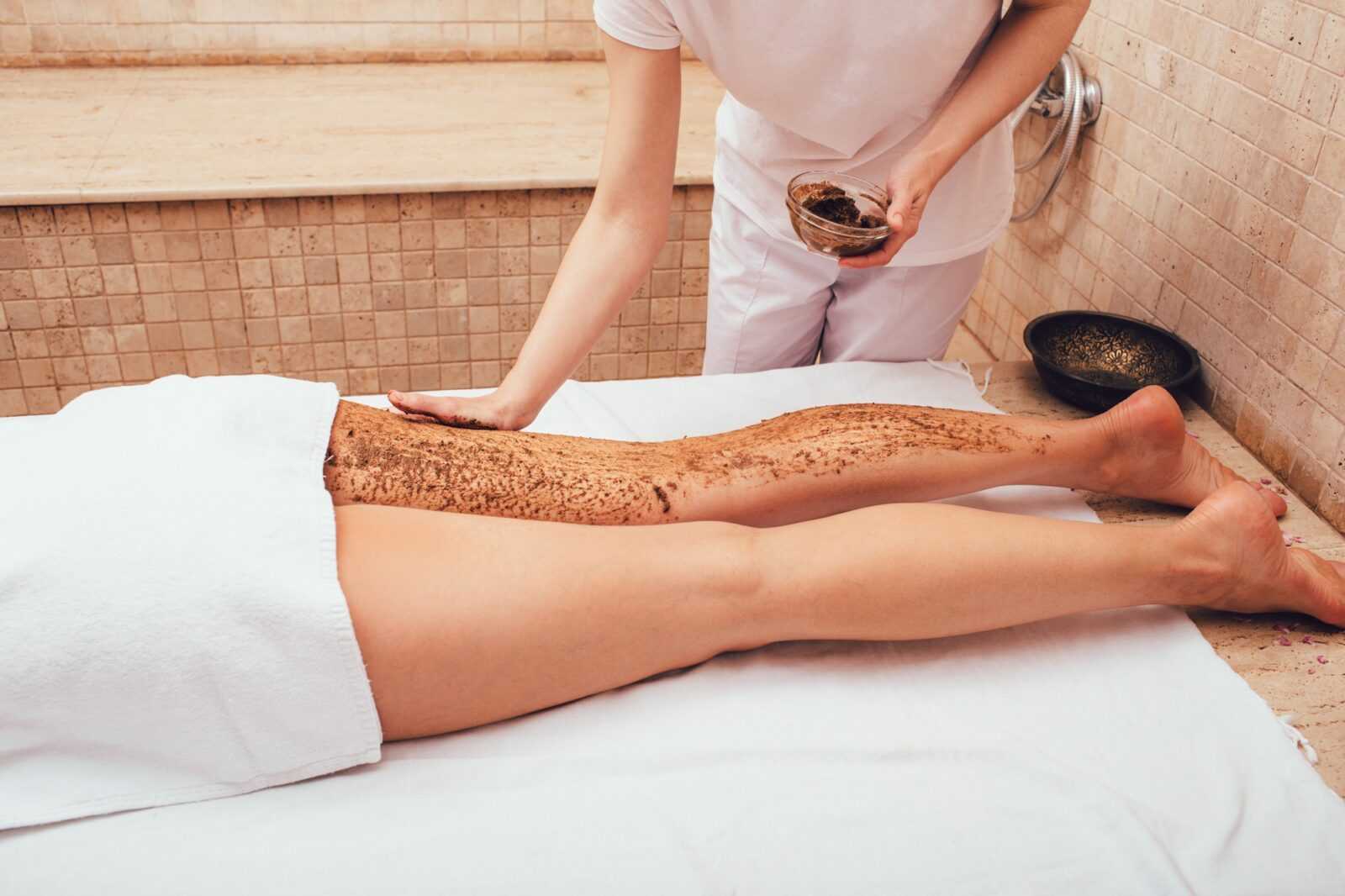 masseur-apply-a-mud-scrub-to-a-woman-s-legs-the-peeling-procedure-for-a-woman-will-make-her-legs
